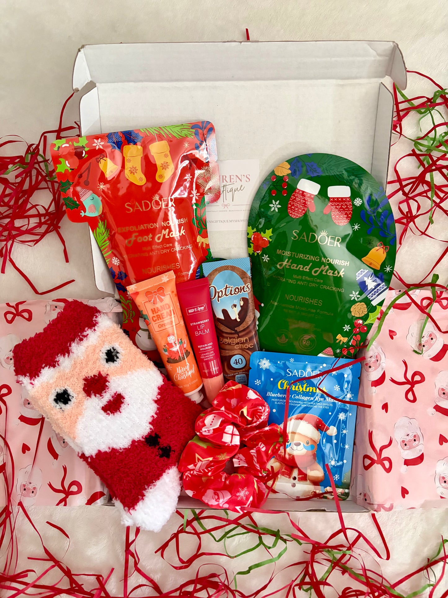 A curated festive self-care box filled with a variety of items such as cosy socks, hand cream, lip balm, eye patches, hand mask, foot mask, hair scrunchie & hot chocolate sachet