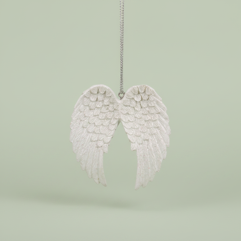 A white angel wing hanging ornament suspended by a silver string against a soft, light sage green background