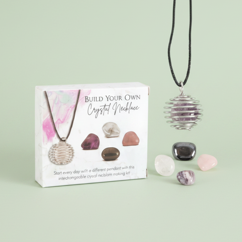 Crystal pendant necklace kit with a silver metallic ball pendant on a black cord, shown next to its printed packaging box and several loose decorative stones on a plain sage green background.