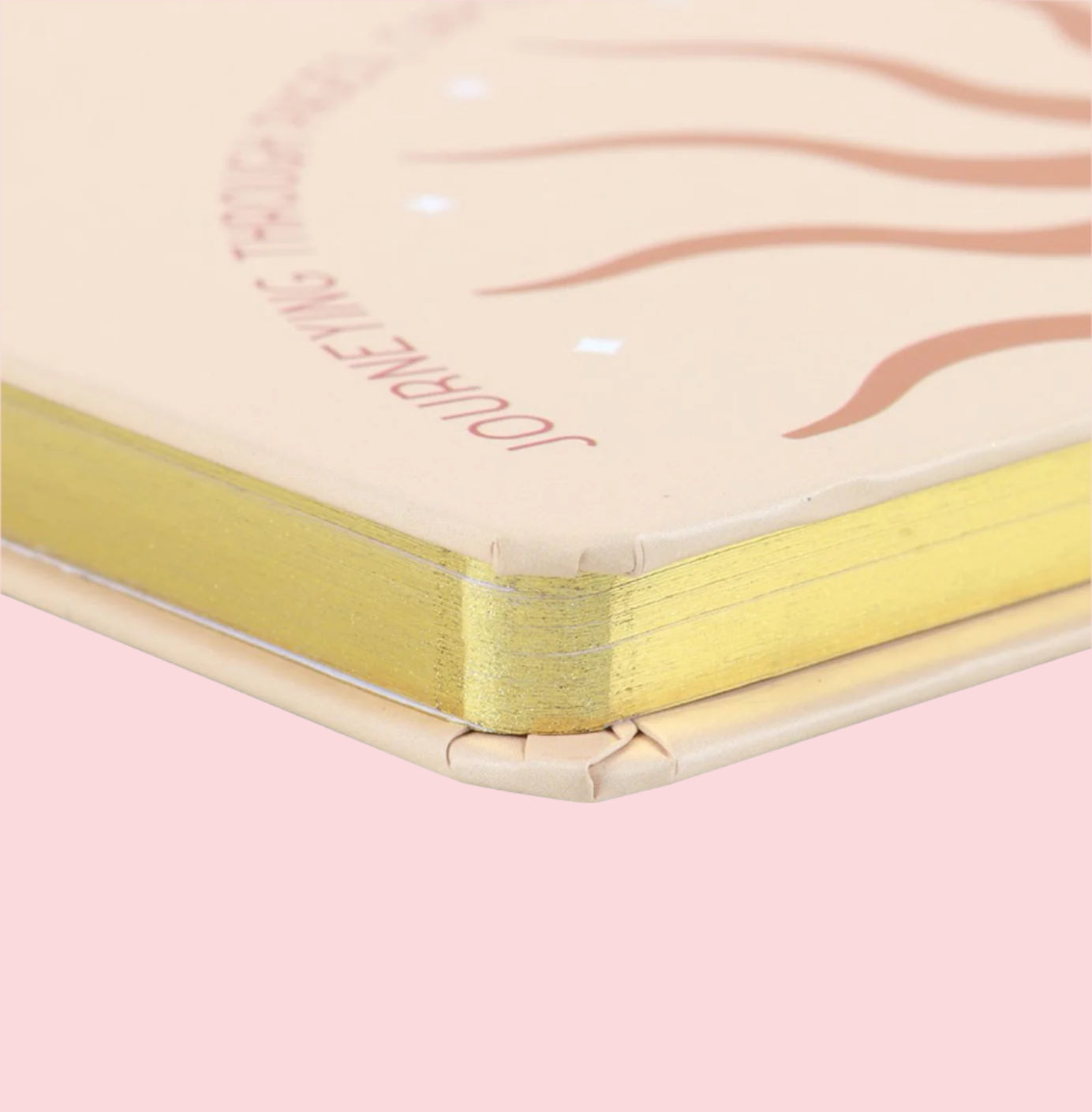 Close-up of a notebook with gold binding and 'Surrounding' branding on a pink background