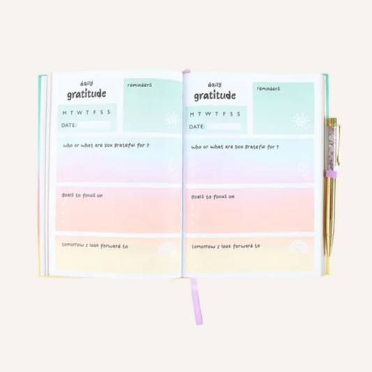 An open pastel gratitude planner page spread with soft mint, pink, peach, and cream colored sections, shown on a plain ivory background.