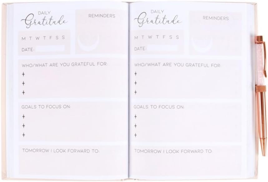 An open white daily gratitude planner with printed sections for reflections, goals, and reminders, shown with a rose-gold pen on the right side.