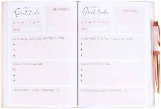 An open white daily gratitude planner with printed sections for reflections, goals, and reminders, shown with a rose-gold pen on the right side.