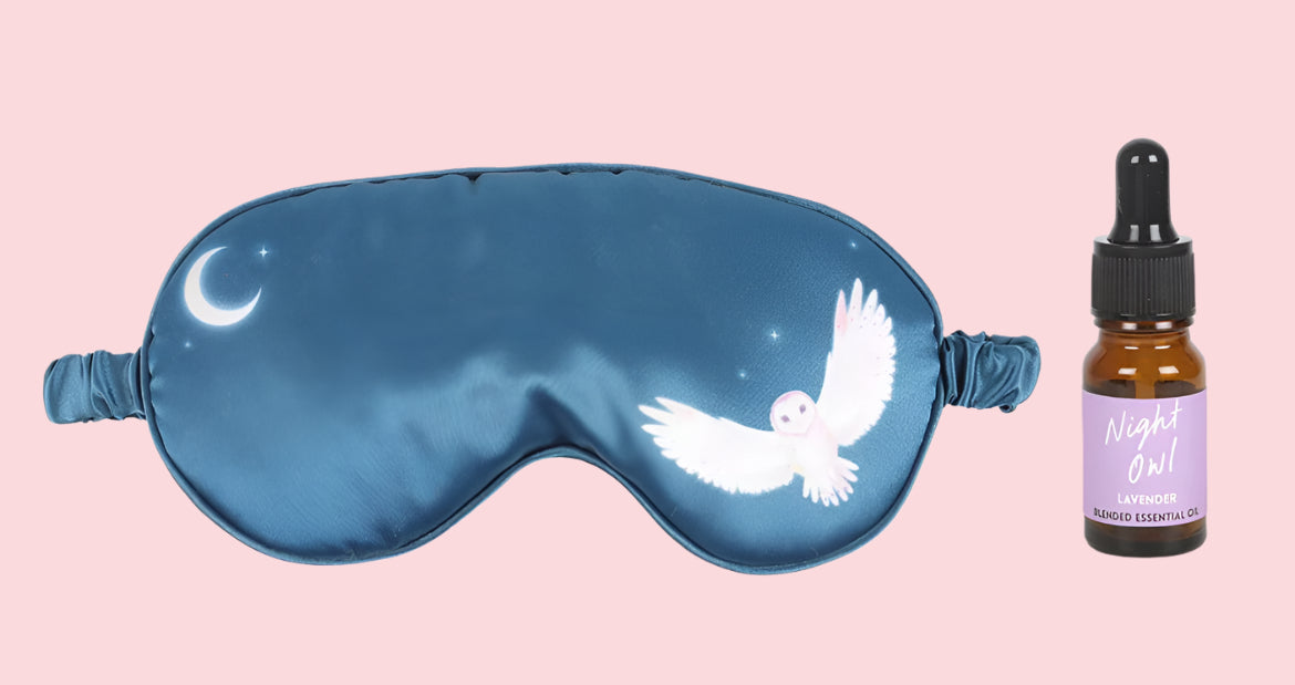 Blue sleep mask with white owl design and a bottle of lavender essential oil
