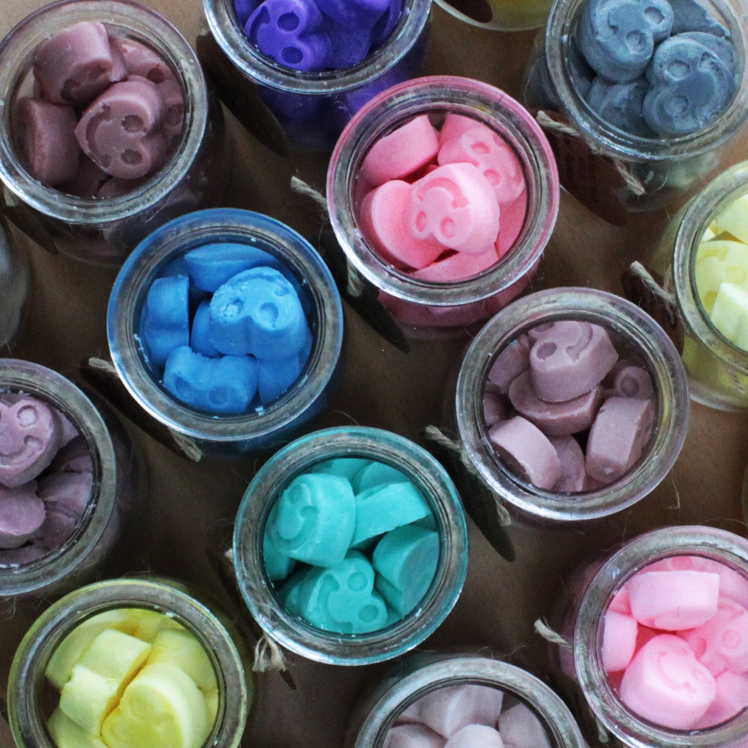 Jars filled with colorful wax melt pieces on a wooden surface