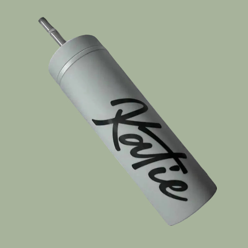 Gray tumbler with 'Katie' written in black cursive on a light green background