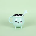 Mint green mug with a face, star-shaped handle, and black interior on a green background