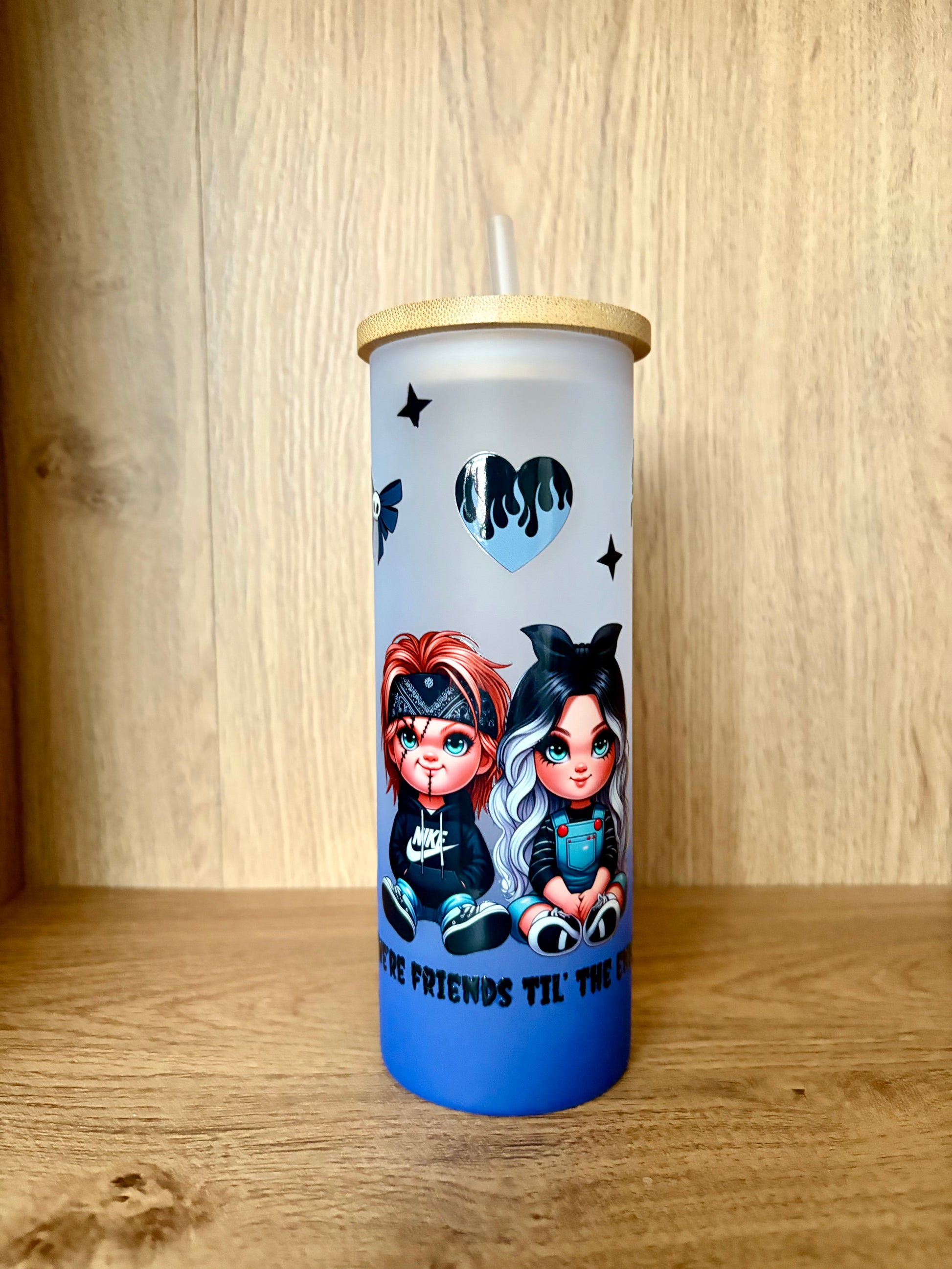 A tall insulated tumbler with a bamboo lid and clear straw, featuring cartoon chibi characters and a blue gradient base, set against a wooden background.