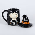 Black mug with a witch design and matching witch hat lid on a grey background