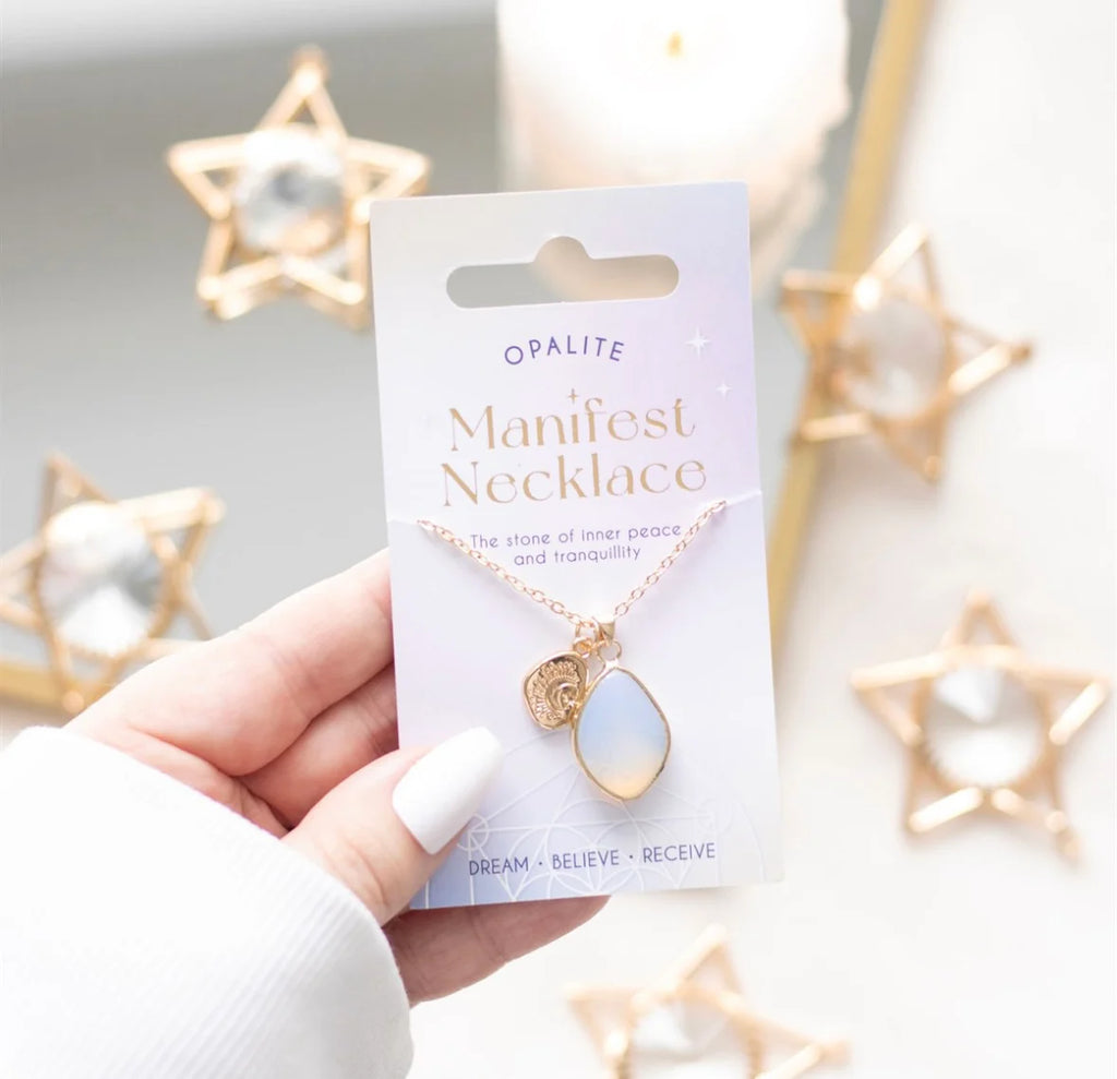 Opalite Manifest Necklace packaging held by a hand with decorative star lights in the background