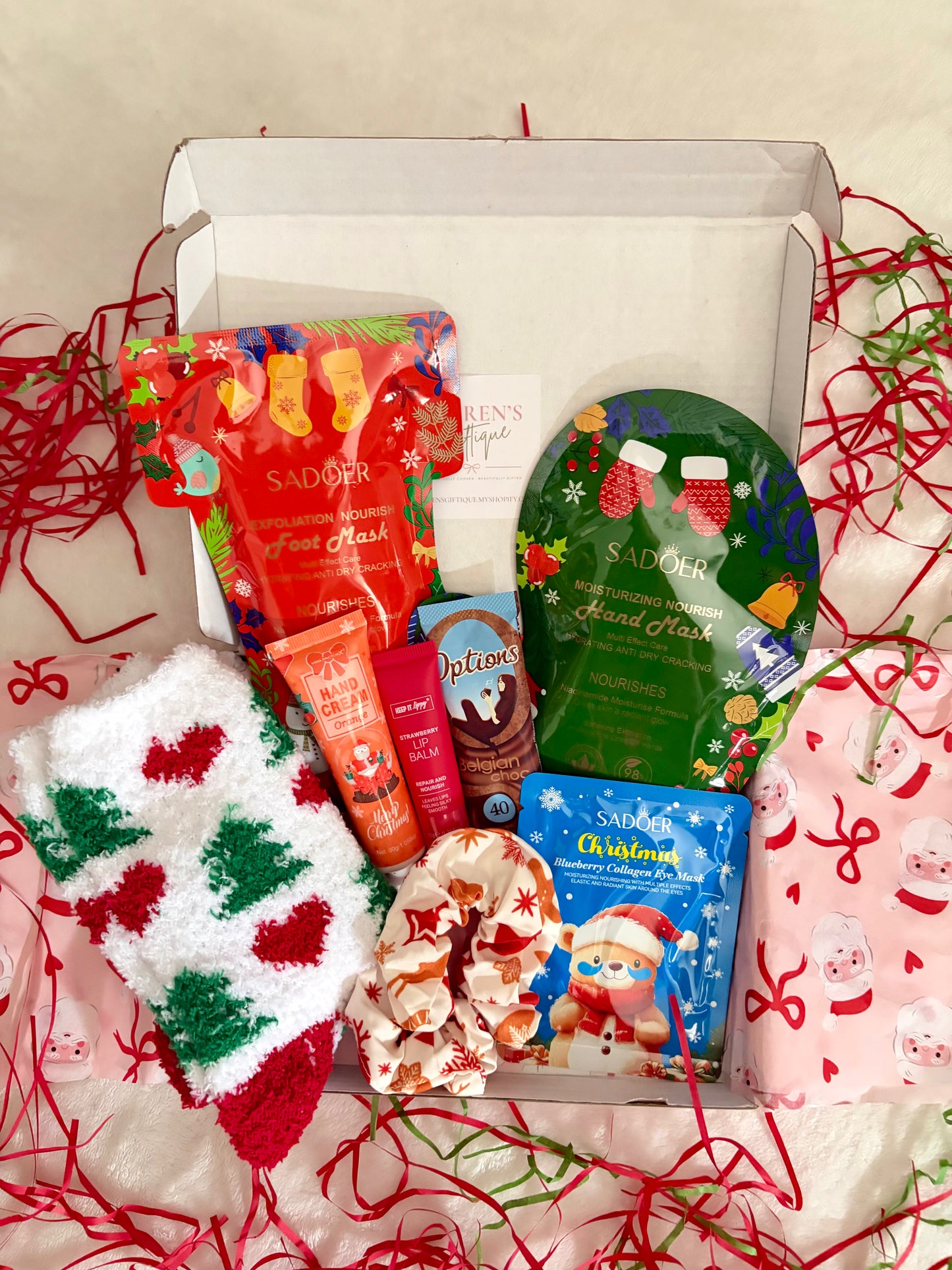 A curated festive self-care box filled with a variety of items such as cosy socks, hand cream, lip balm, eye patches, hand mask, foot mask, hair scrunchie & hot chocolate sachet