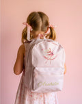 Girl wearing a backpack with a floral design and 'Arabella' printed on it against a pink background