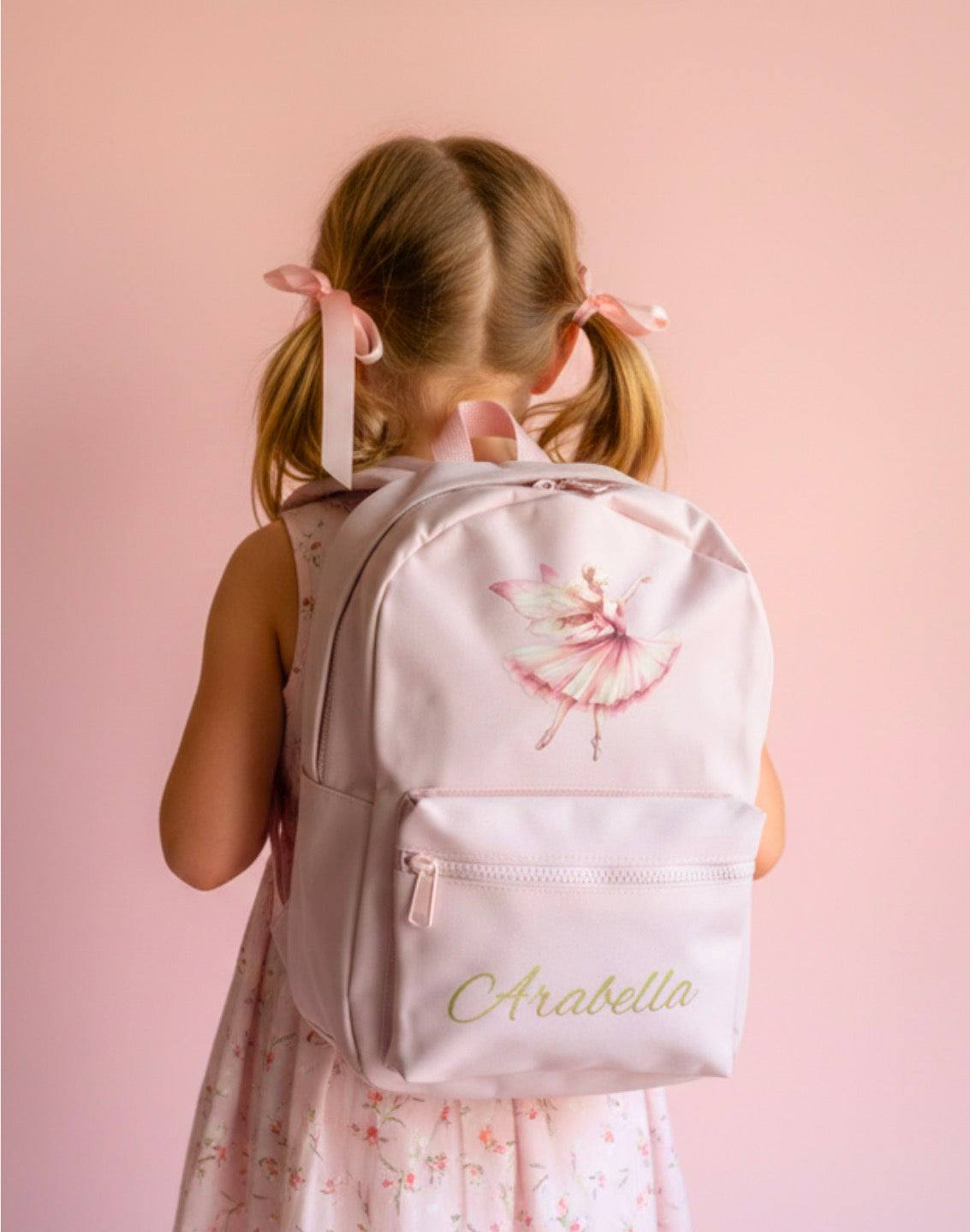 Girl wearing a backpack with a floral design and 'Arabella' printed on it against a pink background