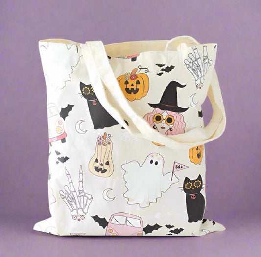 An off-white canvas tote bag with a cute Halloween print featuring pumpkins, ghosts, cats, a witch hat, bats, and skeleton hands, set against a solid purple background.