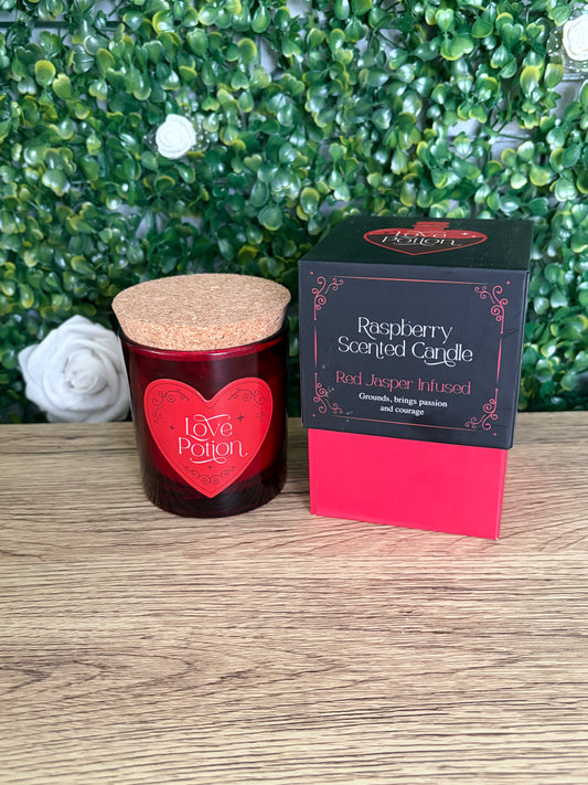 Raspberry scented candle box ed jasper infused with red glass jar and cork lid on a wooden surface with a green leafy backdrop