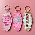 Three pink keychains with motivational phrases on a pink background