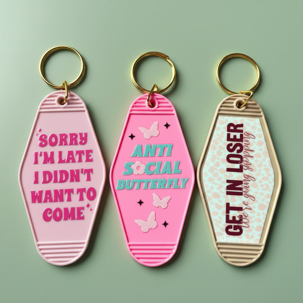 Three pink keychains with motivational phrases on a pink background