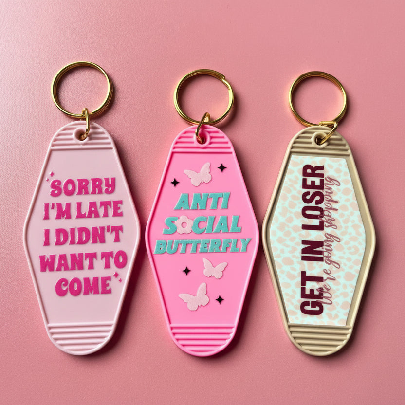 Three pink keychains with motivational phrases on a pink background