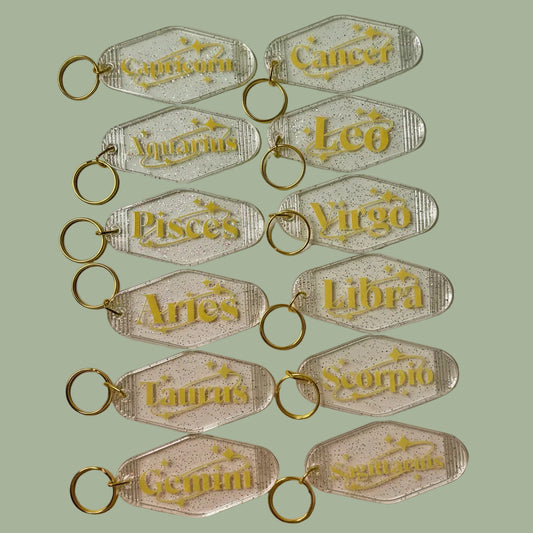 Set of zodiac keychains with gold text on a white background