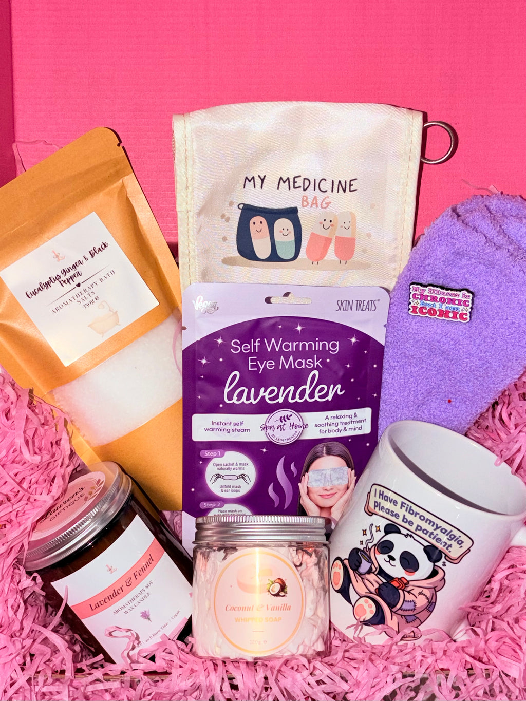Collection of self-care products including a self-warming eye mask, candle, and mug on a pink background.