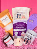 Collection of self-care products including a self-warming eye mask, candle, and mug on a pink background.