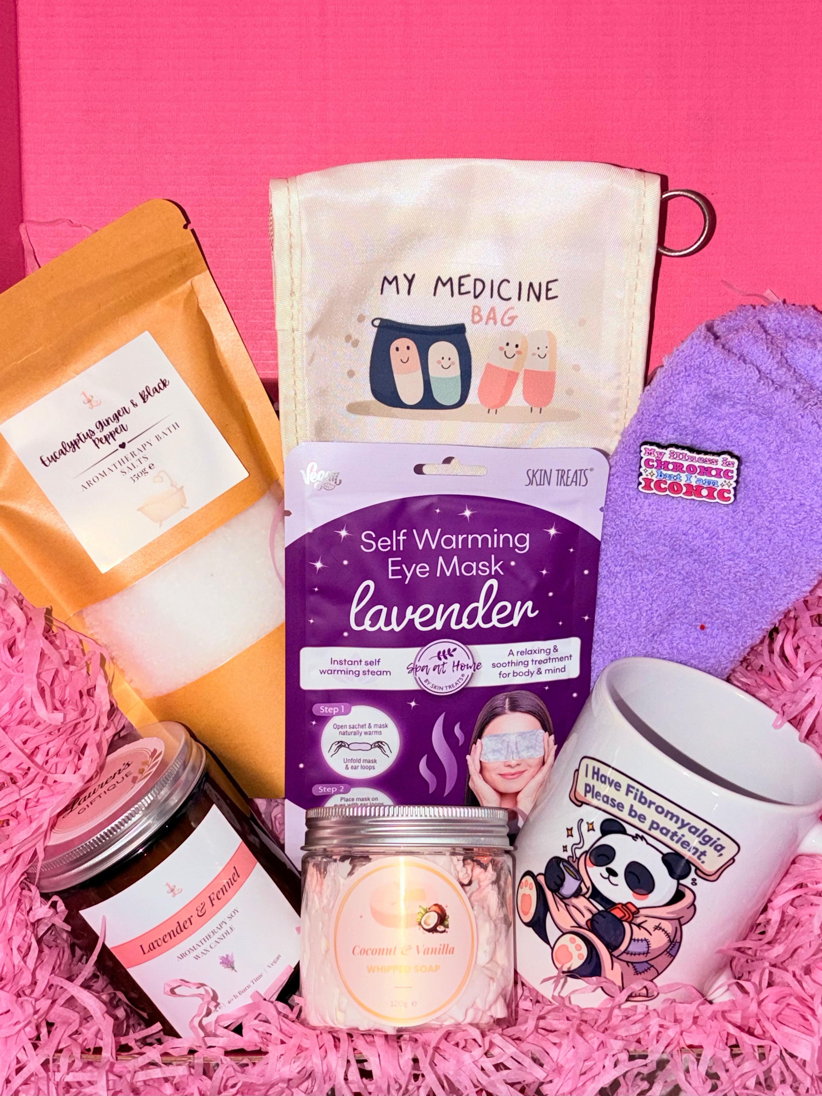 Collection of self-care products including a self-warming eye mask, candle, and mug on a pink background.