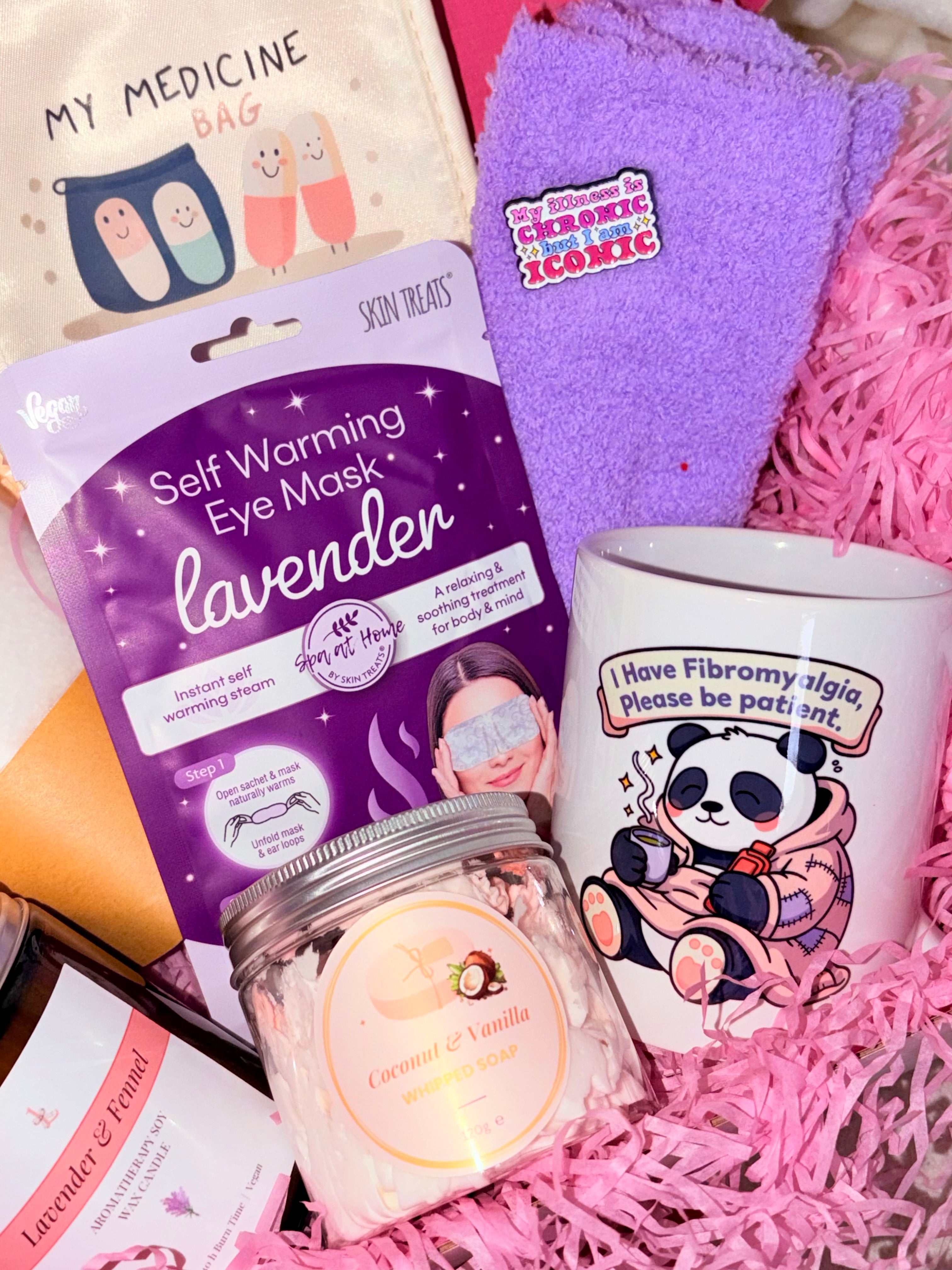 Collection of self-care items including an eye mask, candle, and mug on a pink textured surface.