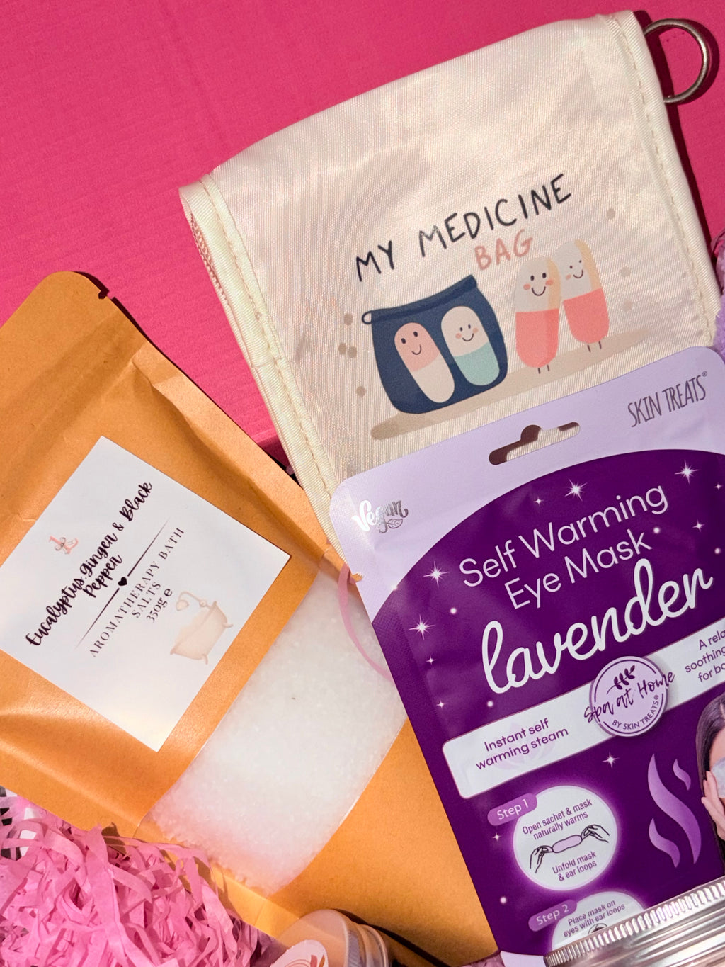 Self-warming eye mask with packaging and a decorative bag on a pink background
