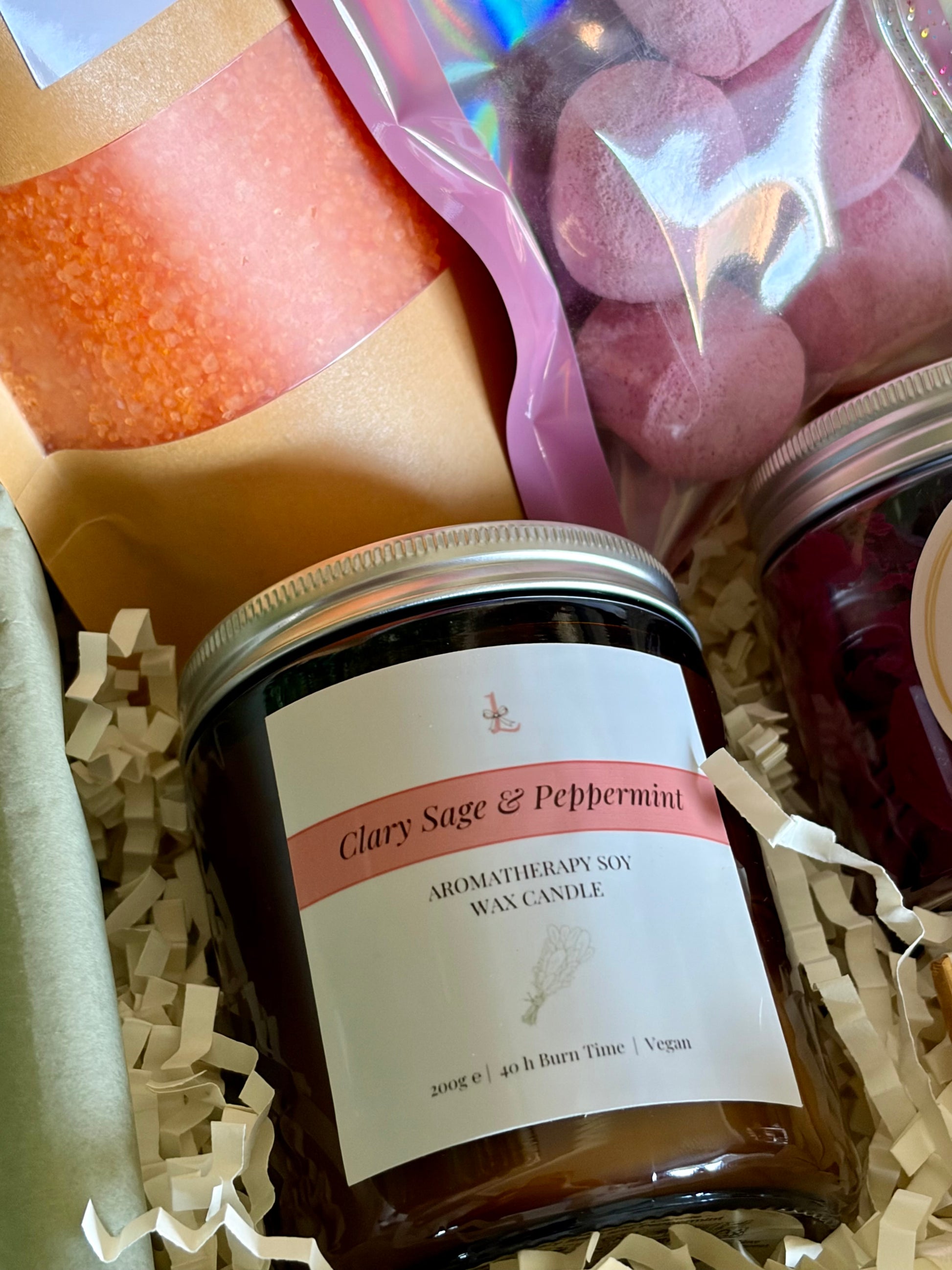 clary sage & peppermint aromatherapy glass jar candle on cream crinkled paper and edging of other bath products.