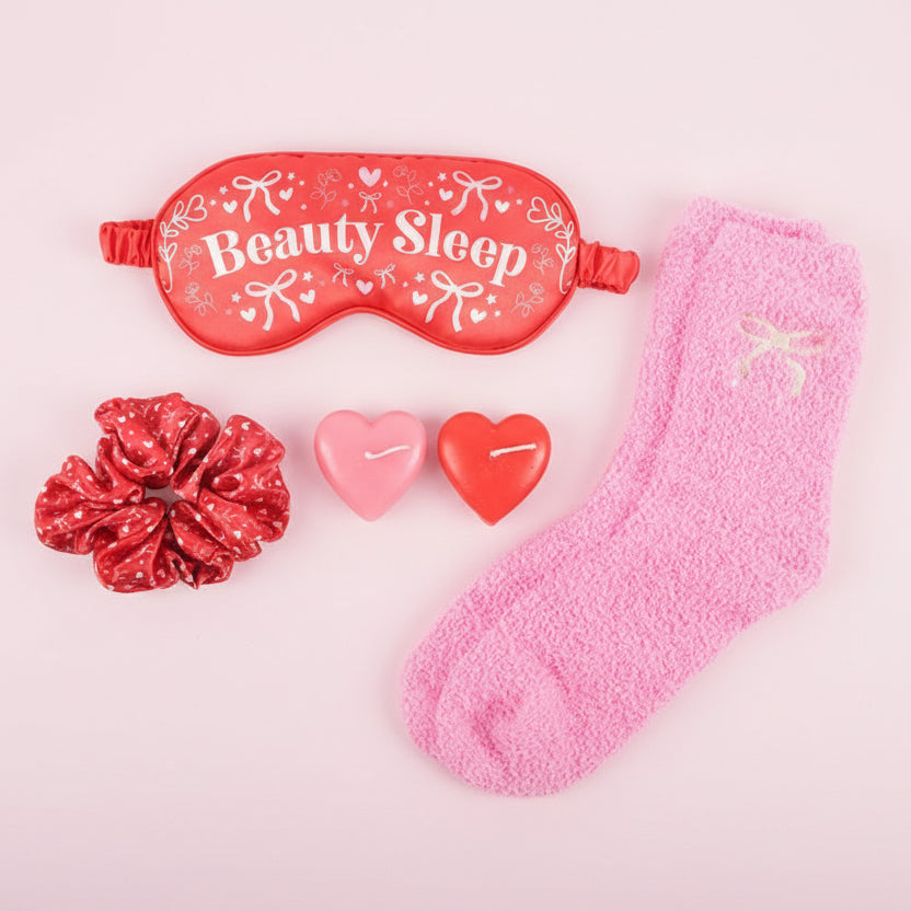 Red sleep mask, socks, scrunchie, and heart-shaped candles on a light background