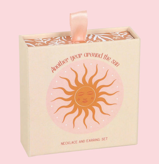 Necklace and earring set packaging with sun design and text on a pink background