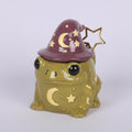 Ceramic frog-shaped mug with a witch hat and star spoon on a light purple background