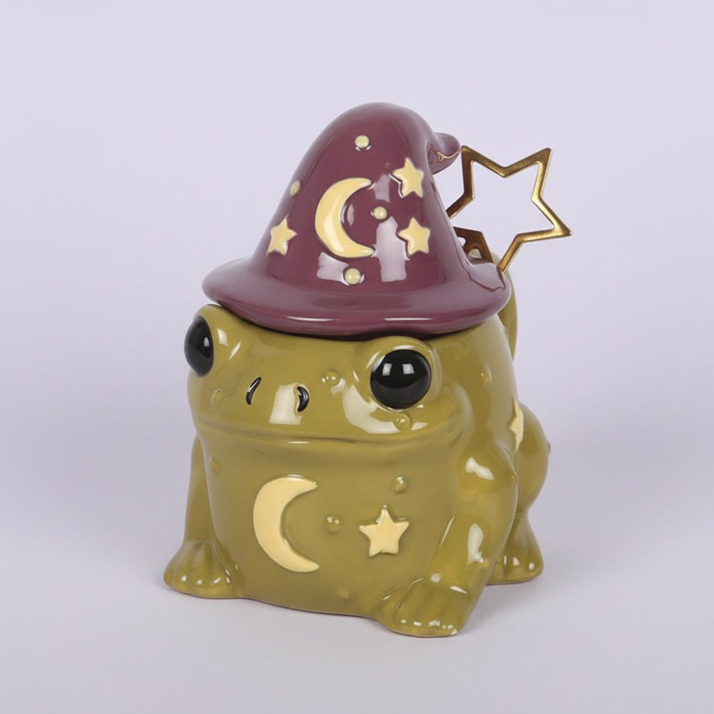 Ceramic frog-shaped mug with a witch hat and star spoon on a light purple background