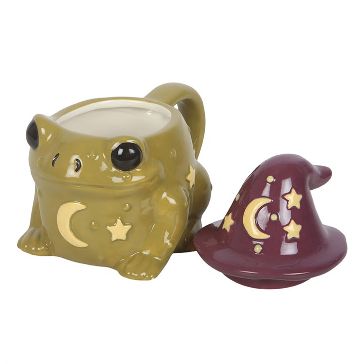 Green frog-shaped mug with star and moon designs, next to a purple witch hat on a white background