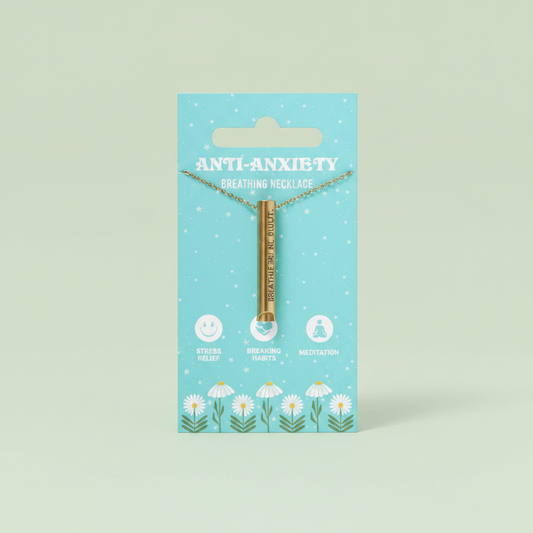 A gold-toned metal necklace with a vertical bar design and small dangling beads, displayed on a light blue card labeled 'ANTI-Anxiety' against a plain sage green background.