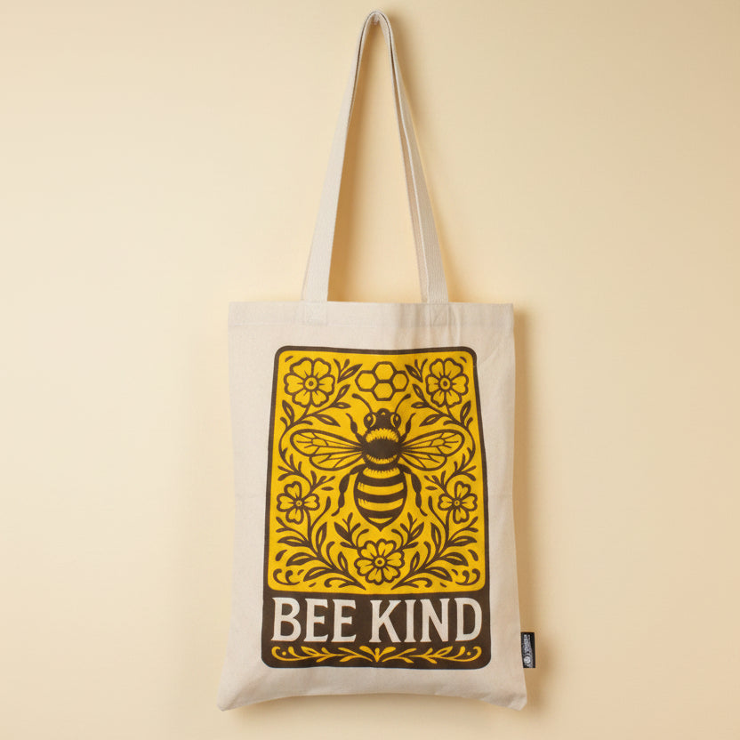 Beige tote bag with a bee and floral design, featuring the text 'BEE KIND', on a yellow background.