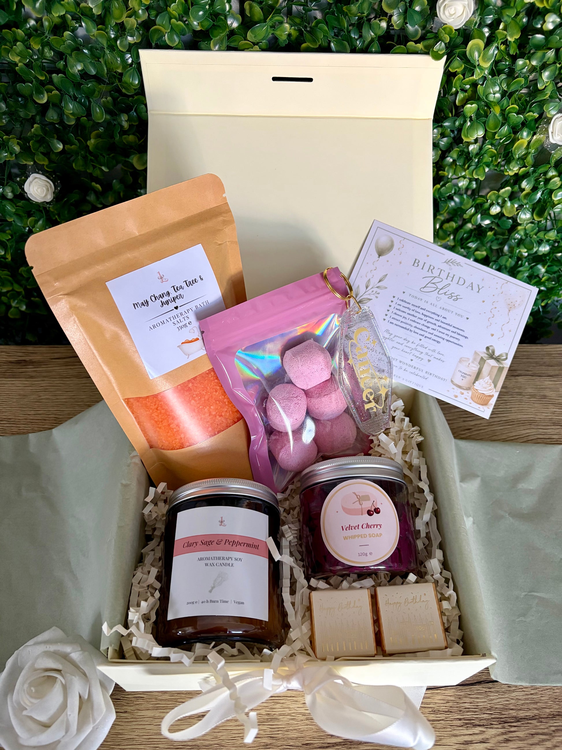birthday bliss gift box with card, bath potion in kraft bag, velvet cherry whipped soap, aromatherapy candle, bath bombs in pouch, zodiac keyring and birthday chocolates in a ivory gift box with green leafy backdrop
