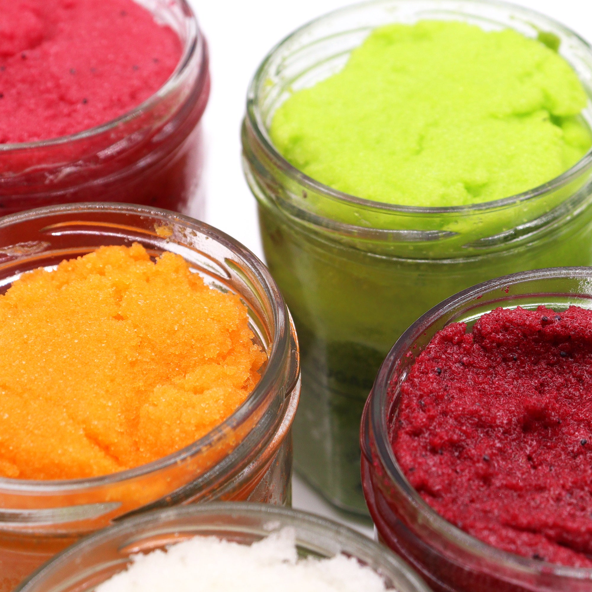 Four jars filled with colorful scrubs in red, green, orange, and white.