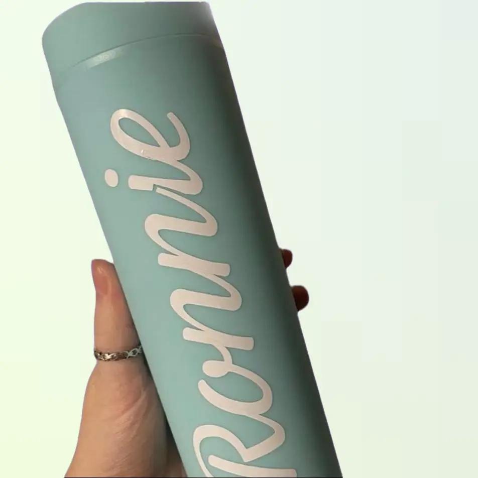 Light blue tumbler with 'Ronnie' printed on it held by a hand against a light green background