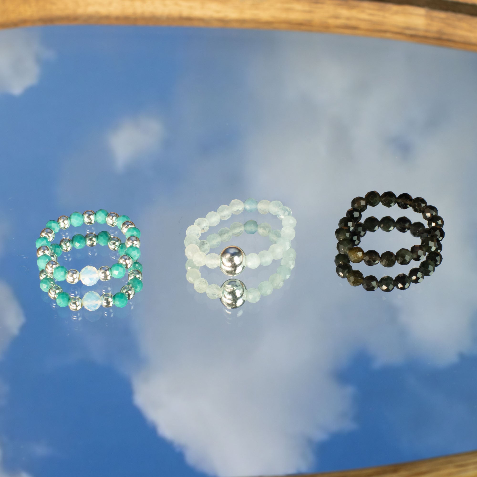 Three gemstone rings on a reflective surface with a blue sky background