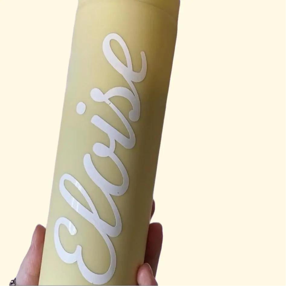 Yellow tumbler with 'Eloise' printed on it held by a hand against a white background