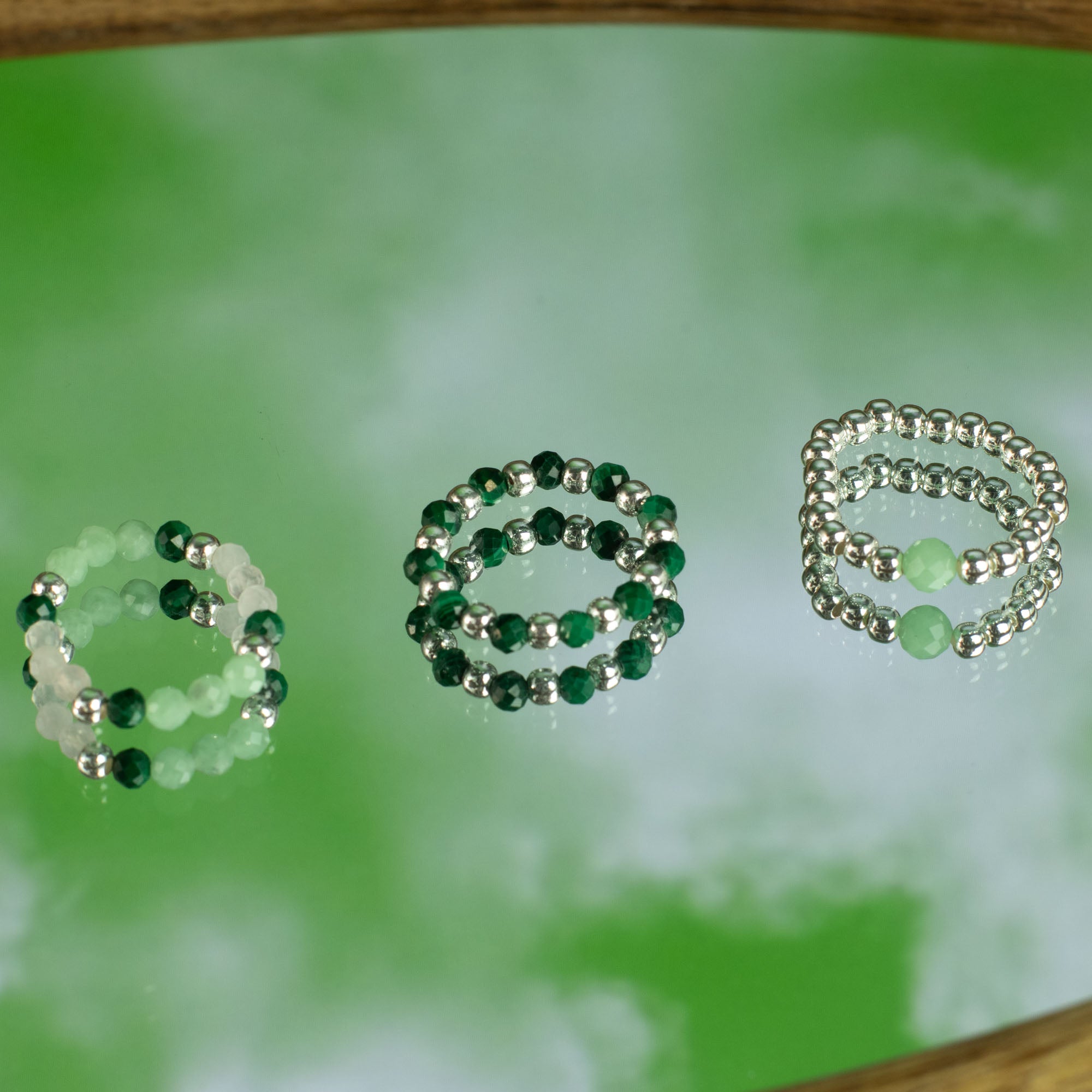Three gemstone rings in green, silver, and a mix of colours on a green background