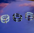 Three gemstone rings on a reflective blue surface with a pinkish hue.