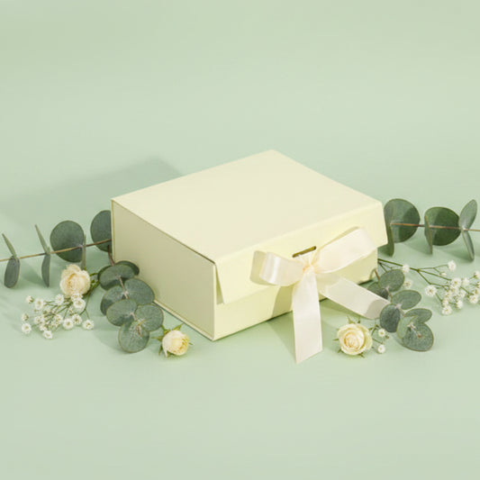 ivory gift box with ribbon on a sage green background with flowers and eucalyptus
