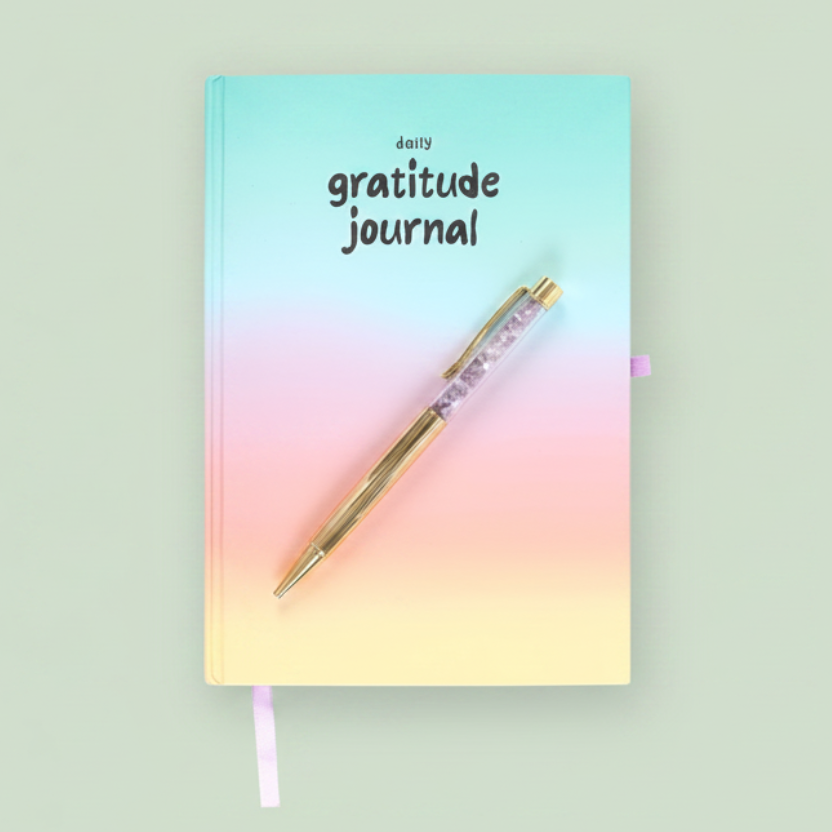 A small gratitude journal with a pastel gradient cover in mint, pink, peach, and pale yellow, featuring a gold pen resting on top, shown against a plain sage green background.
