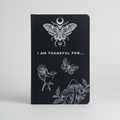 Black notebook with white illustrations of a butterfly, bird, and plants on a grey background