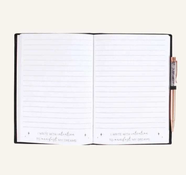 An open lined notebook with a black cover and a rose gold pen tucked on the right side, photographed on a clean ivory background.