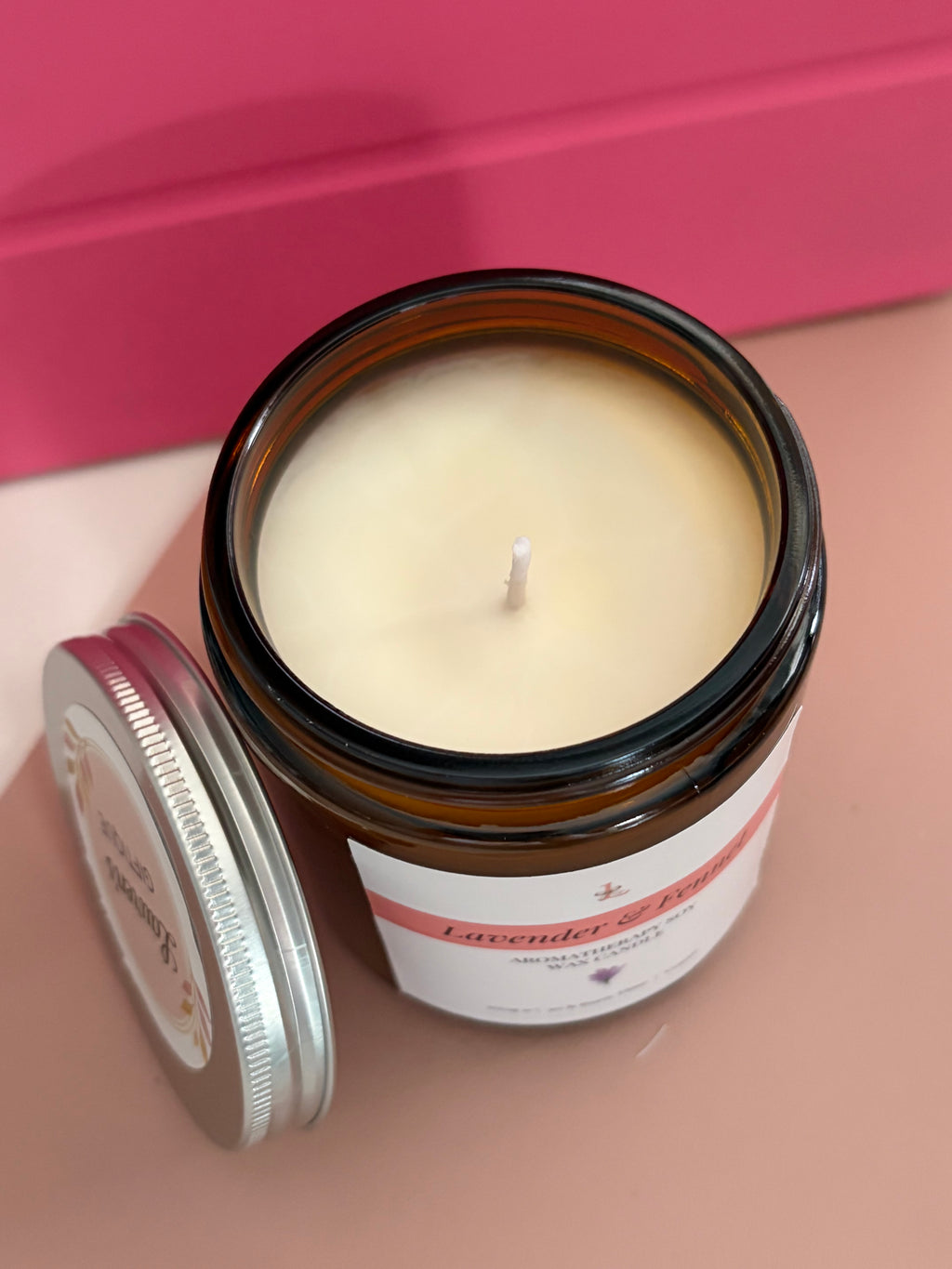 Candle in a glass jar with a label on a pink background