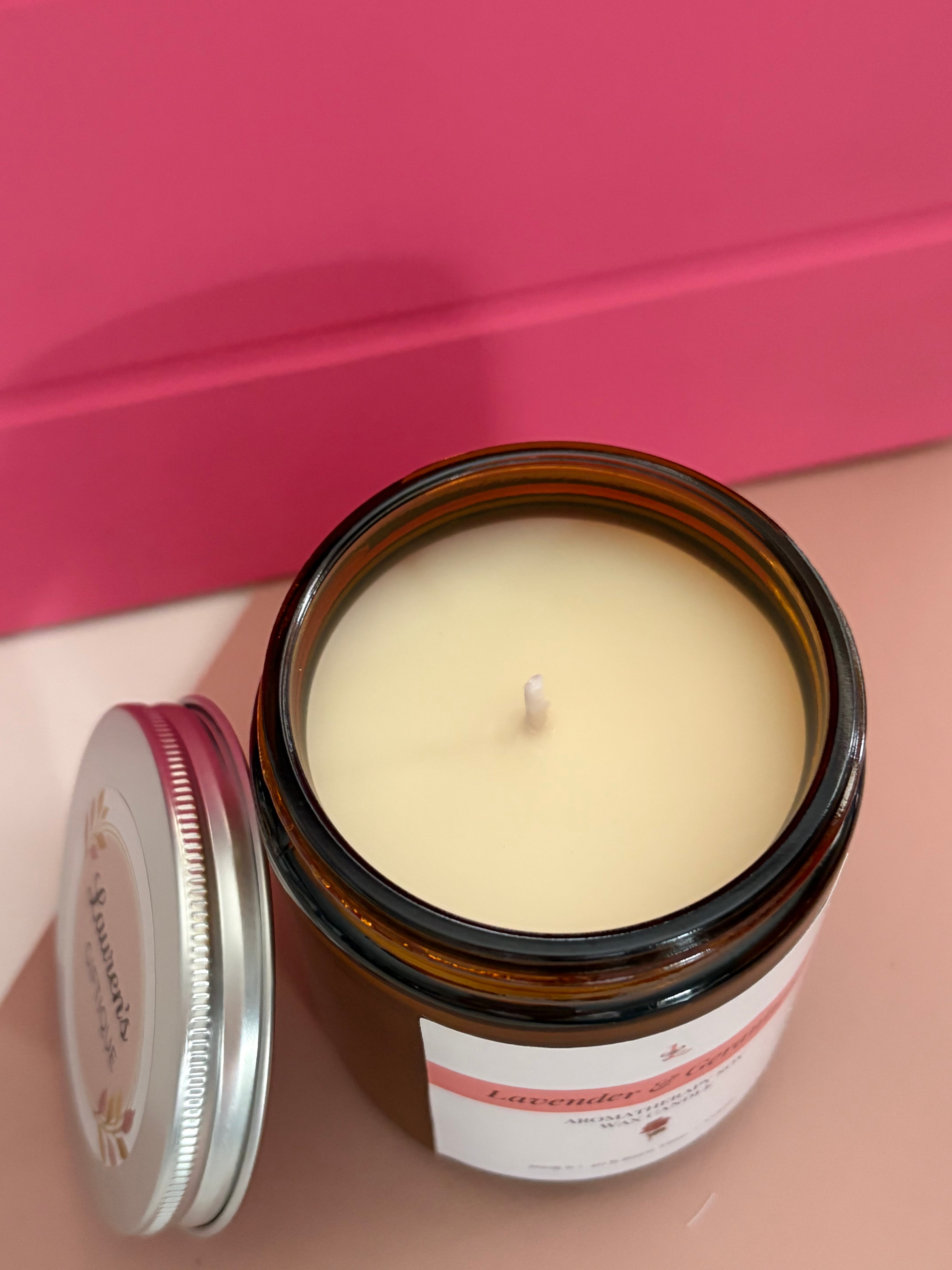 Candle in a brown jar with a visible label on a pink background