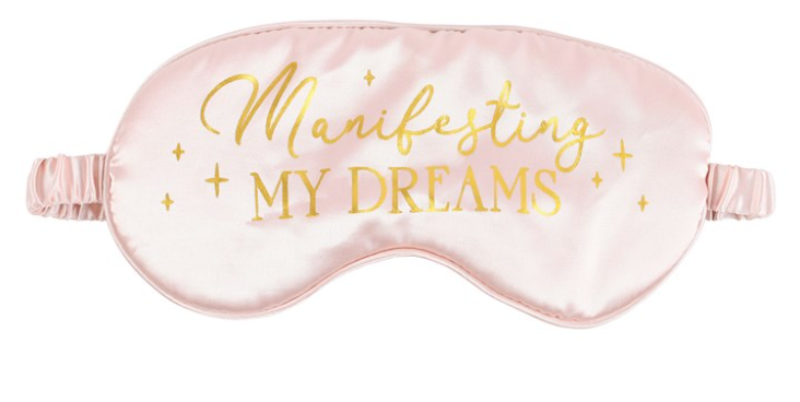 Pink sleep mask with 'Manifesting My Dreams' text in gold on a white background